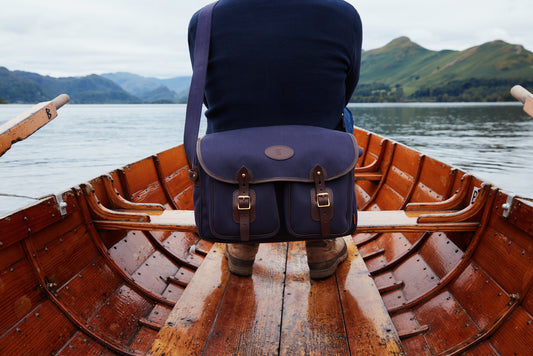 Person sitting in a wooden rowboat on a lake with a blue Chapman Rambler 40 bag over their shoulder.